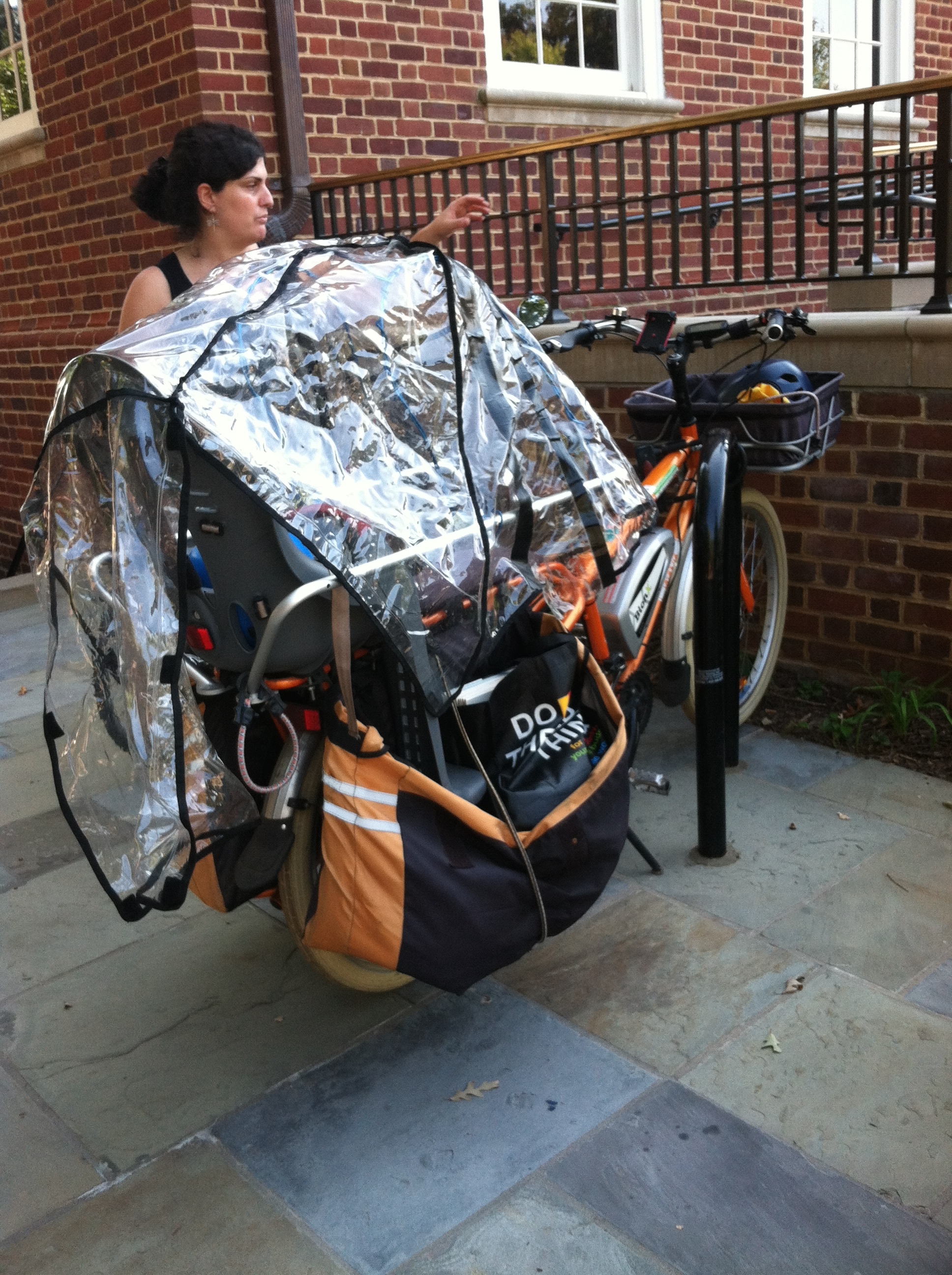 Megan from Kidical Mass D.C. shows off her Yuba cargo bike, with two kids seats, "monkey bars," panniers, and a rain cover.