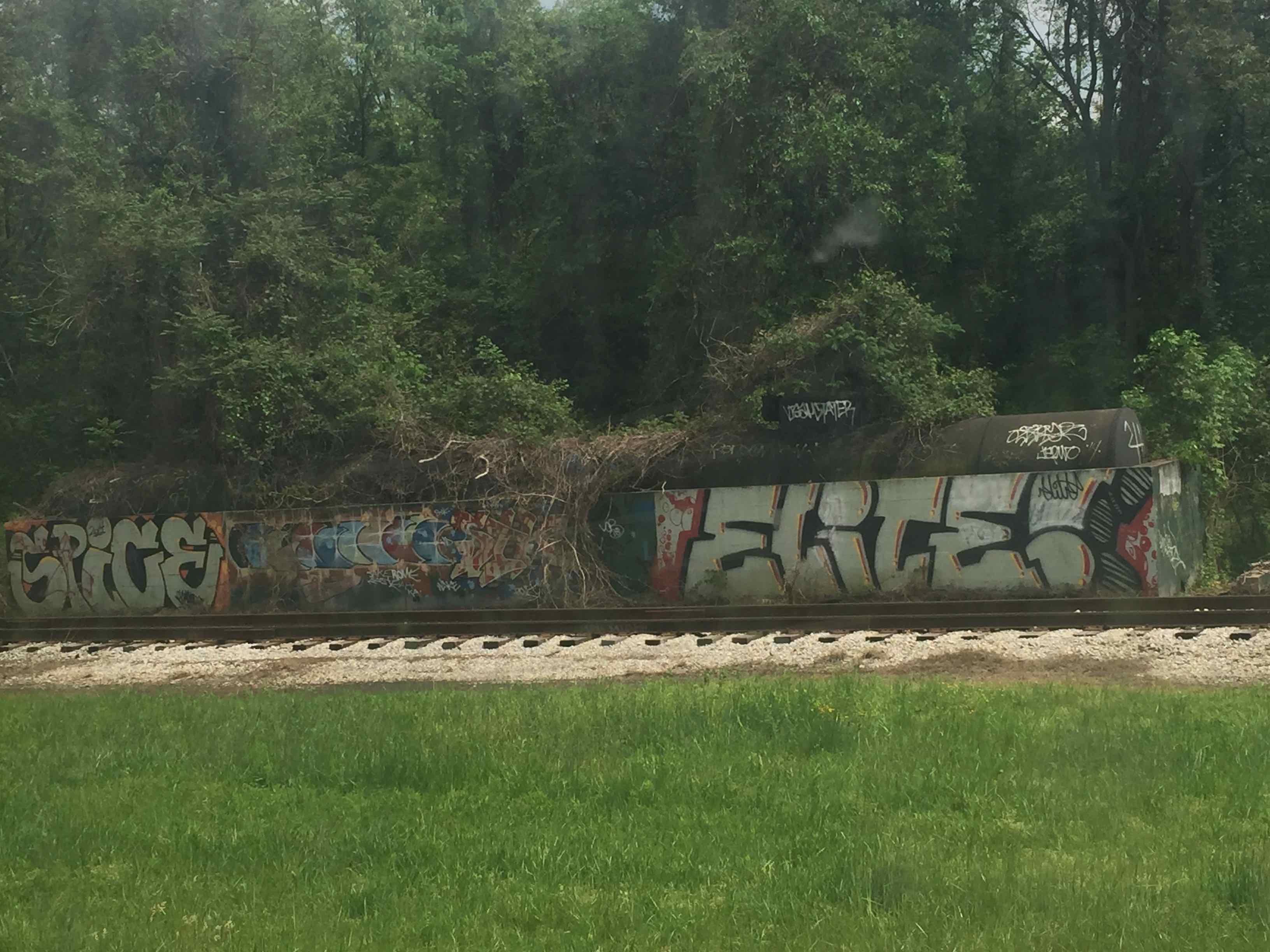 Photo: Rusted out oil tanker covered with graffiti in front of train tracks and grass